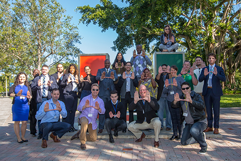 This is a photo of a group of political science students at the University of Miami. The students are standing around the "U" sculpture and a using their hands to gesture the shape of a letter "U."